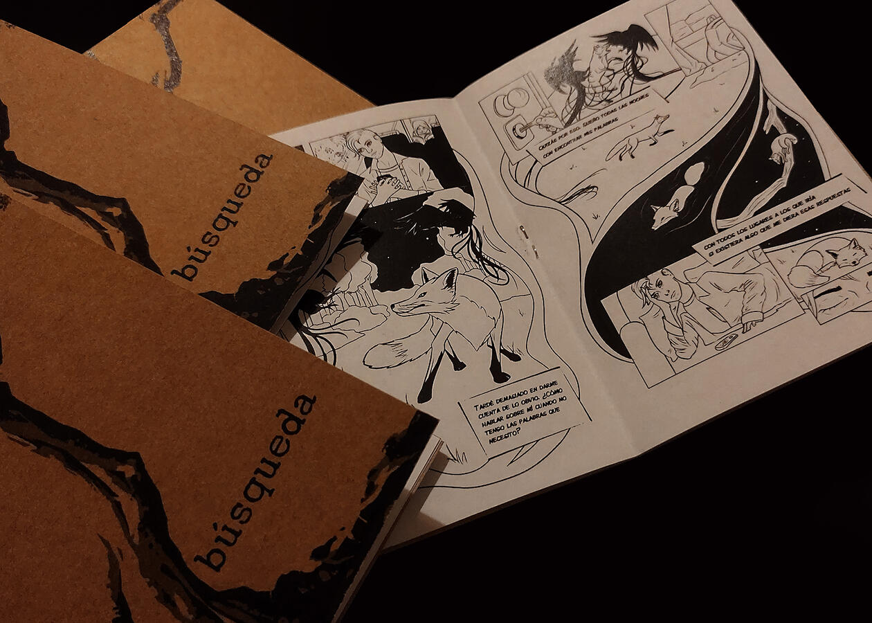 Several copies of a zine piled on a dark background. One of them is opened, showing a sequential spread